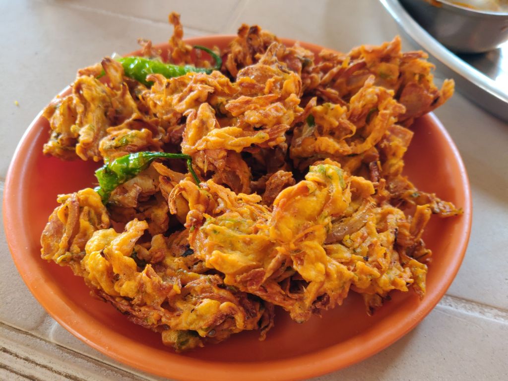 Mit Teig umhüllte Zwiebelringe und grünen Chilis auf einem Teller: das indische Gericht Onion Pakora