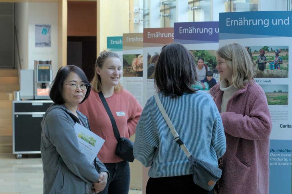 Vier Frauen stehen vor einer Ausstellung bestehend aus fünf Bannern und unterhalten sich.