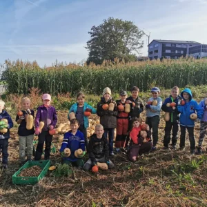 Eine Kindergruppe posiert stolz mit ihren geernteten Kürbissen auf dem Feld.