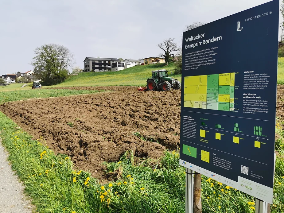 Hinter dem Eingangsschild des Weltackers pflügt ein Traktor den Weltacker. 