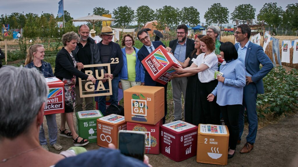 Beim Sommerfest halten Cem Özdemir, das Mannheimer Team, Antonio Andrioli und Weltacker-Gründer Benedikt Hearlin einen Würfel mit der Aufschrift "Weltacker" hoch.