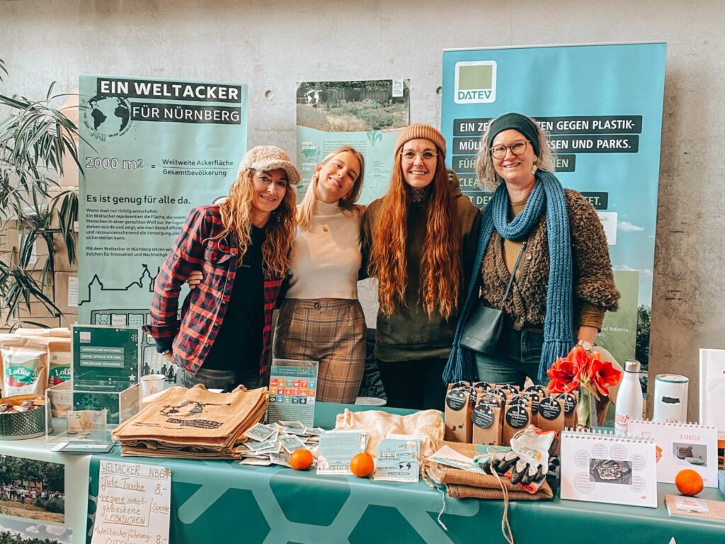 Four members of the Nuremberg Weltacker stand at a market stall and smile into the camera.