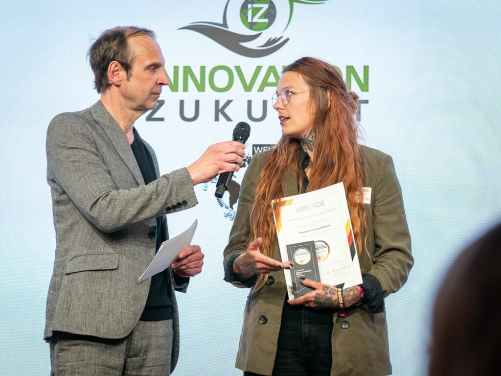 Elna Tietböhl holds the prize in her hands and is interviewed on stage.