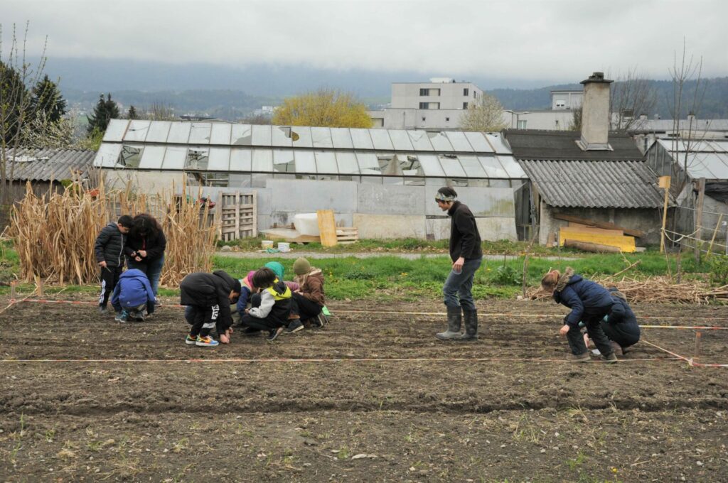 Unter Anleitung sät eine Gruppe von Kindern auf einem abgesteckten Feld des Weltackers. 