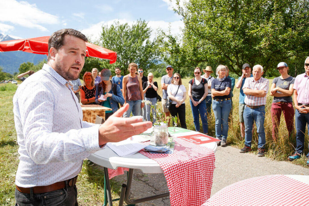 Florian Bernardi hält an kleinen Tischen auf dem Ernährungsfeld Vaduz einen Vortrag. Eine Gruppe Erwachsener lauscht gespannt.