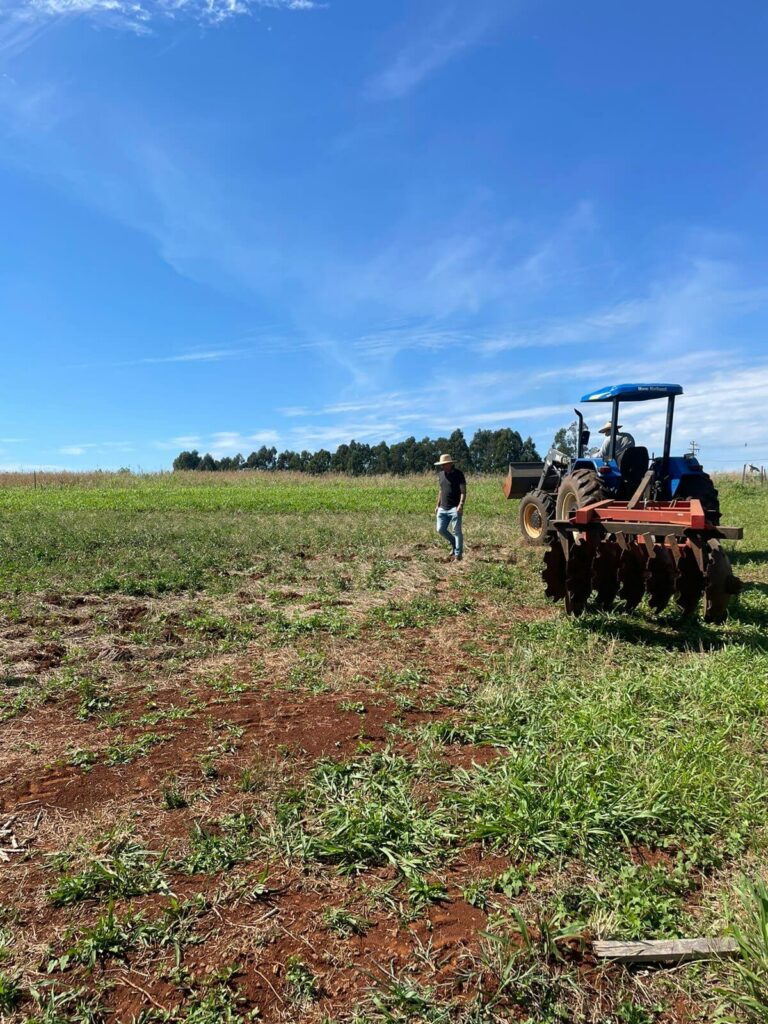 A man is walking in front of a tractor and checking out the field.