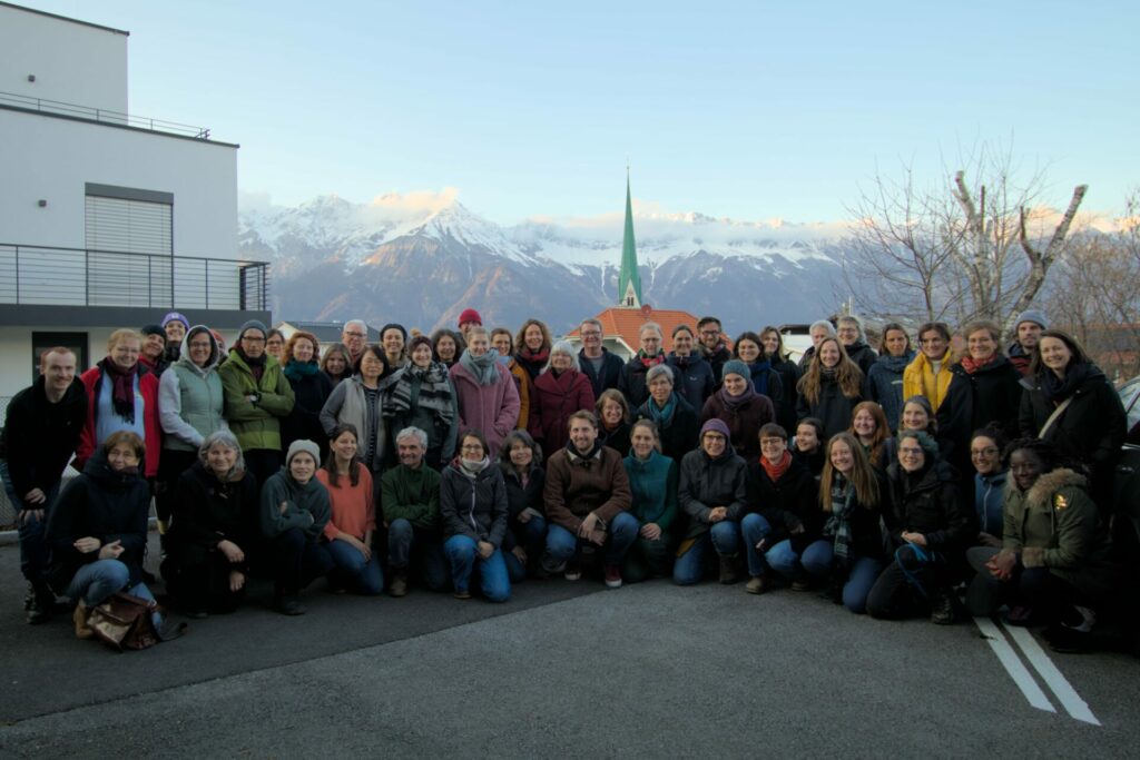 Fast 60 Teilnehmende der Konferenz in Innsbruck blicken für ein Gruppenfoto in die Kamera. Im Hintergrund sind die schneebedeckten Alpen zu sehen. 