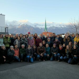 Fast 60 Teilnehmende der Konferenz in Innsbruck blicken für ein Gruppenfoto in die Kamera. Im Hintergrund sind die schneebedeckten Alpen zu sehen.