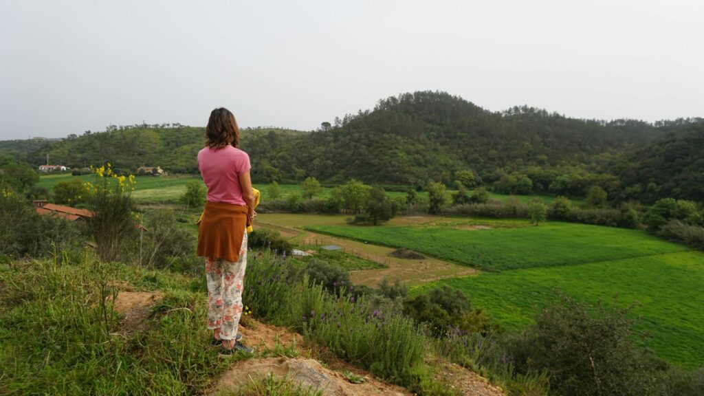 A woman is standing on a hill and looking down on a field of grass.