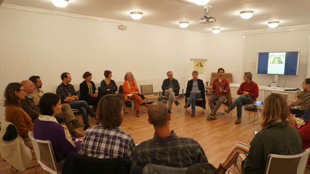 Approximately 20 people sit in a circle in a room and discuss the development of Campo Global. 