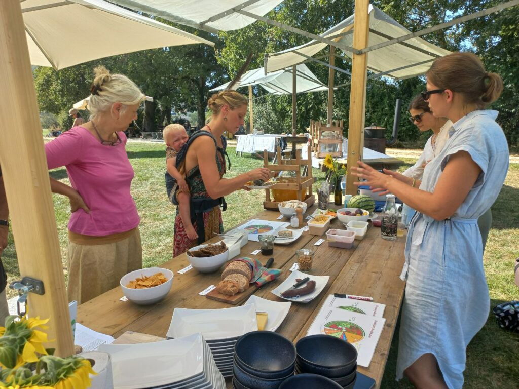 Personen unterhalten sich an einem Buffet über die Planetary Health Diet. Auf dem Tisch liegen auch Informationen zur Planetary Health Diet.