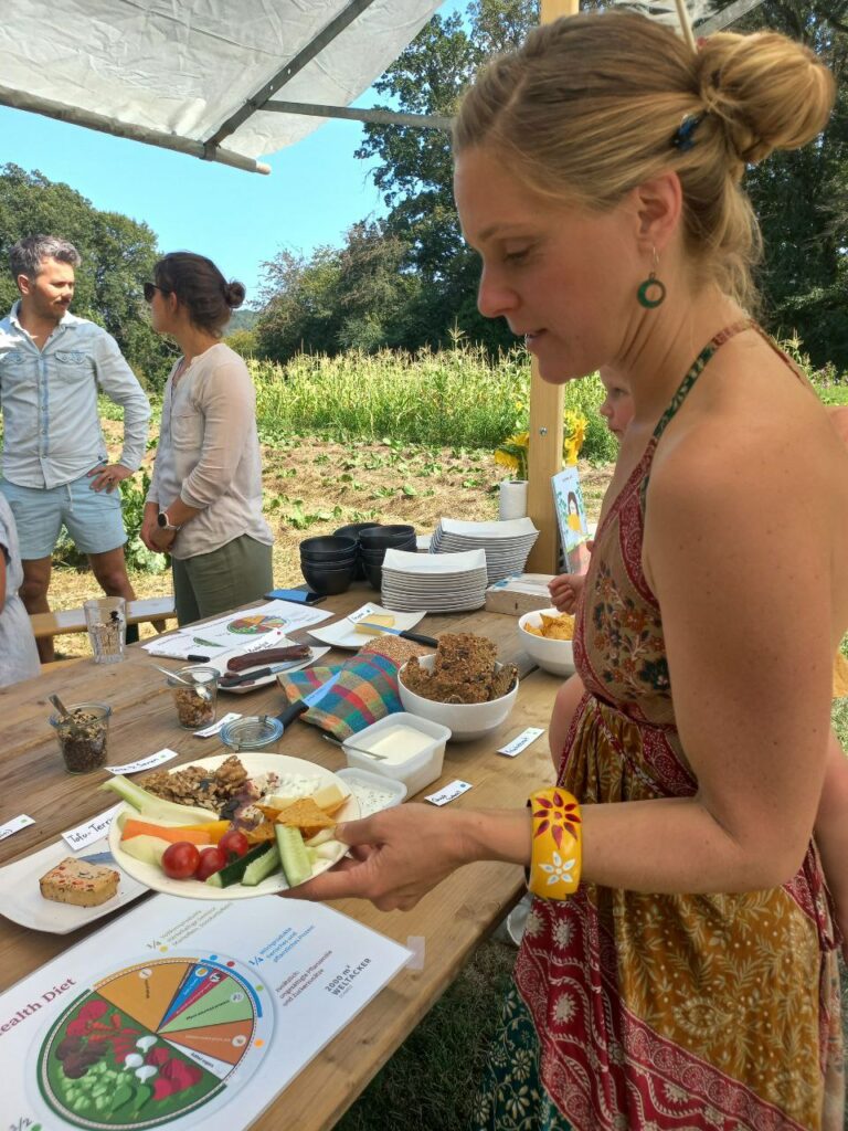 Eine Frau schöpft sich an einem vollen Buffet einen Teller während zwei andere Personen im Hintergrund zusammen sprechen.