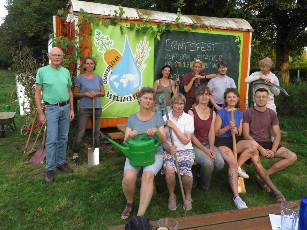 Das Team vom Weltacker Osnabrück steht vor ihrem Bauwagen. Alle haben Ackergeräte in den Händen. 