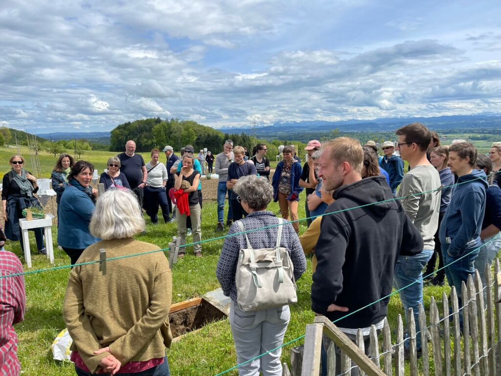 Eine Gruppe Menschen steht um eine Bodenluke und lauscht Rosmarie bei ihren Ausführungen. 