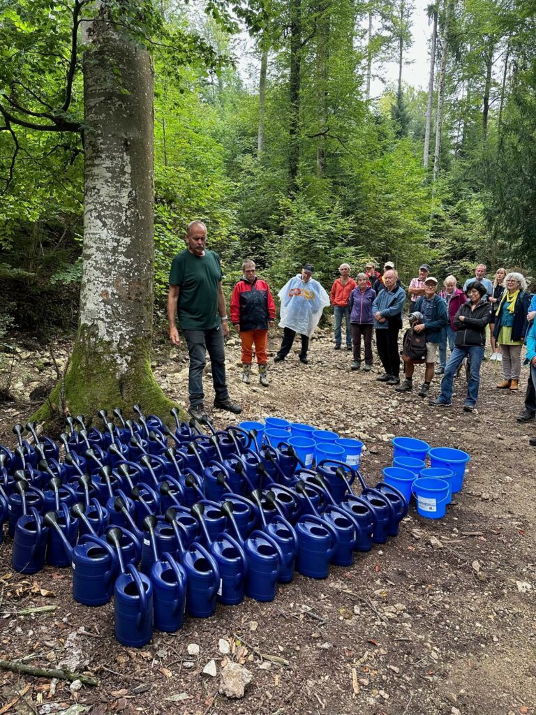 Der Ackerleiter Peter leitet die Wassertragen-Aktion an, wo Menschen mithilfe von Eimern und Gießkannen, eine solidarische Wassertragen-Aktion durchführen. 