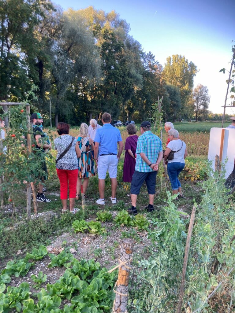 Eine Gruppe Erwachsener folgt gespannt der Weltackertour, während sie auf einem Weg zwischen den Feldern stehen.