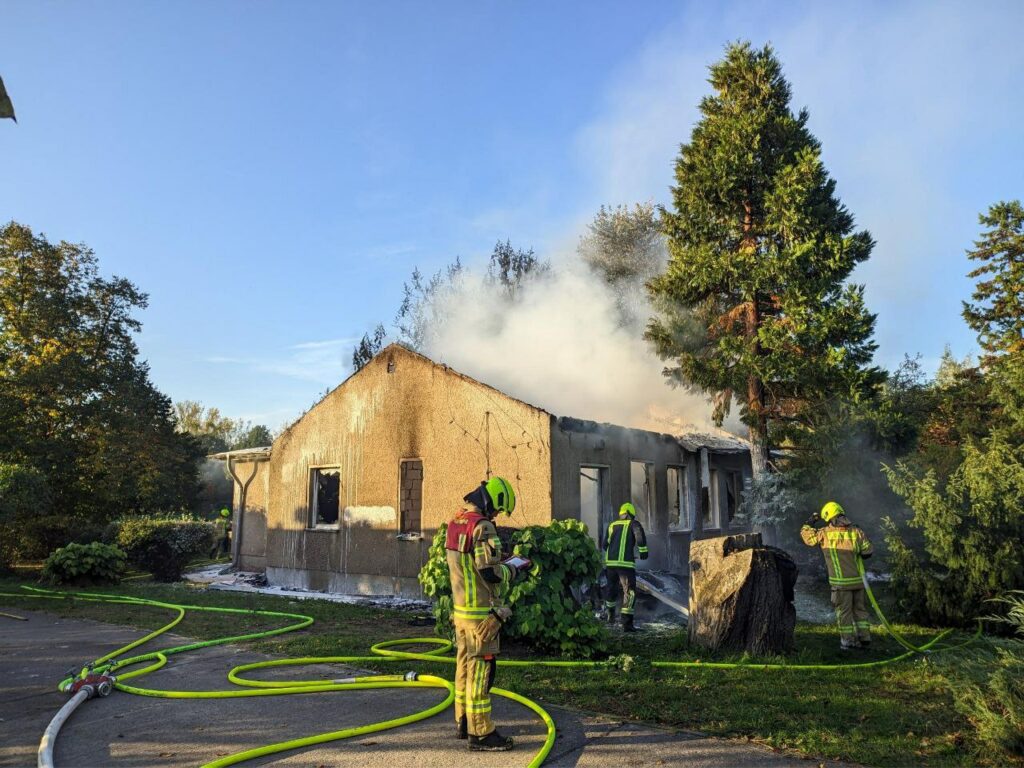 In the morning, smoke is still rising above the burnt-down house. Three members of the fire department are using hoses to continue the extinguishing work.