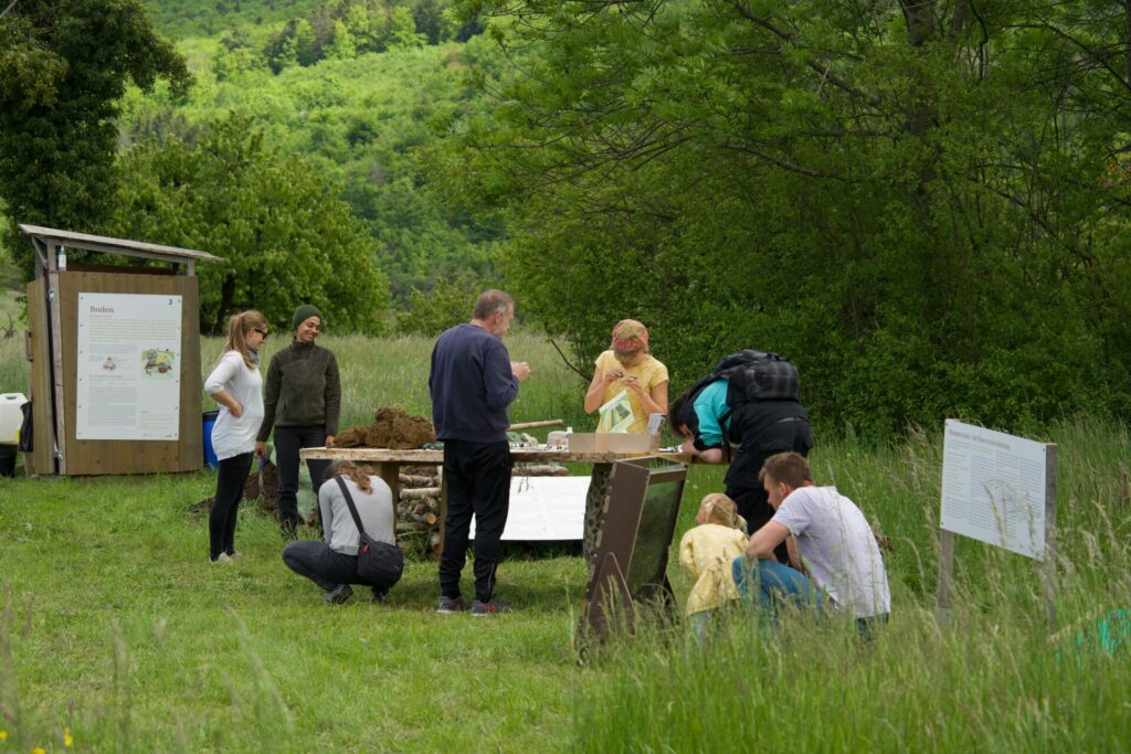 Several adults sit at the table and look at a floor table, a child explores the root window.