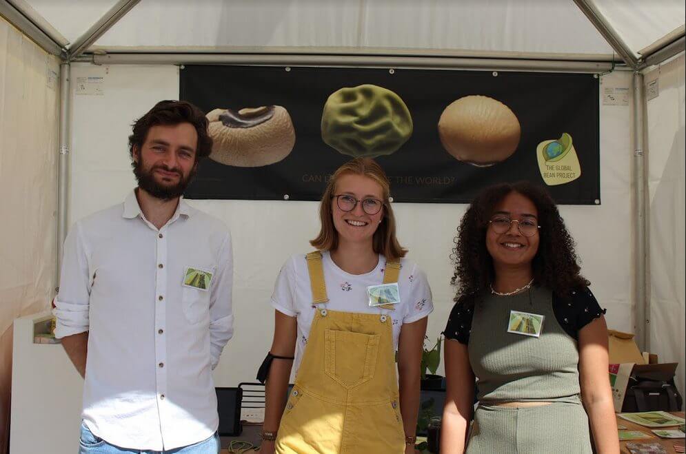 Three employees of the Global Bean Project stand in front of the Global Bean information table.